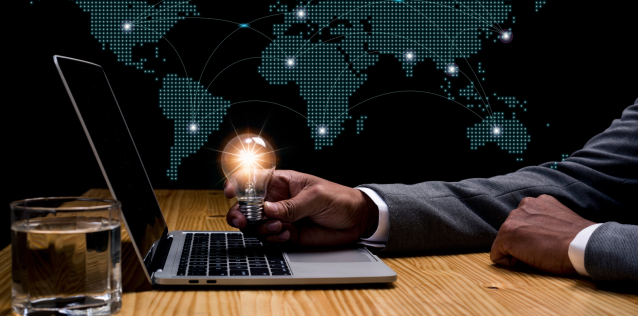 Lightbulb floats above a laptop with a tech map of the United States behind it. A man sits in front of the laptop.